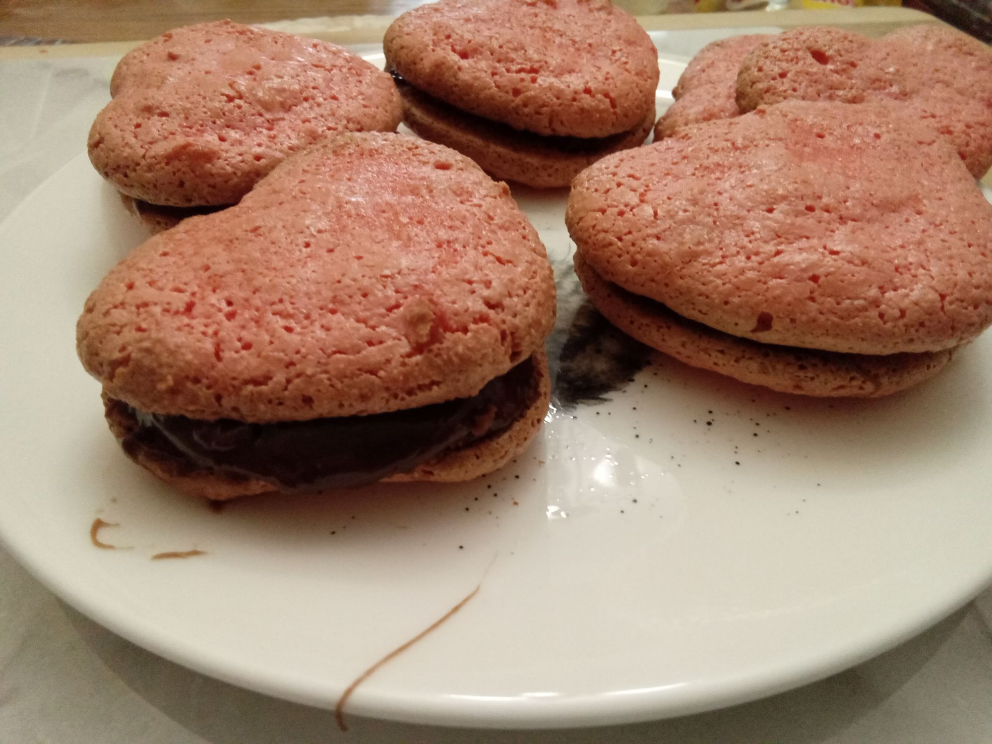 Petite assiette vue de profil, remplis de macarons parisien rosés en forme de coeur avec caramel au chocolat au centre.